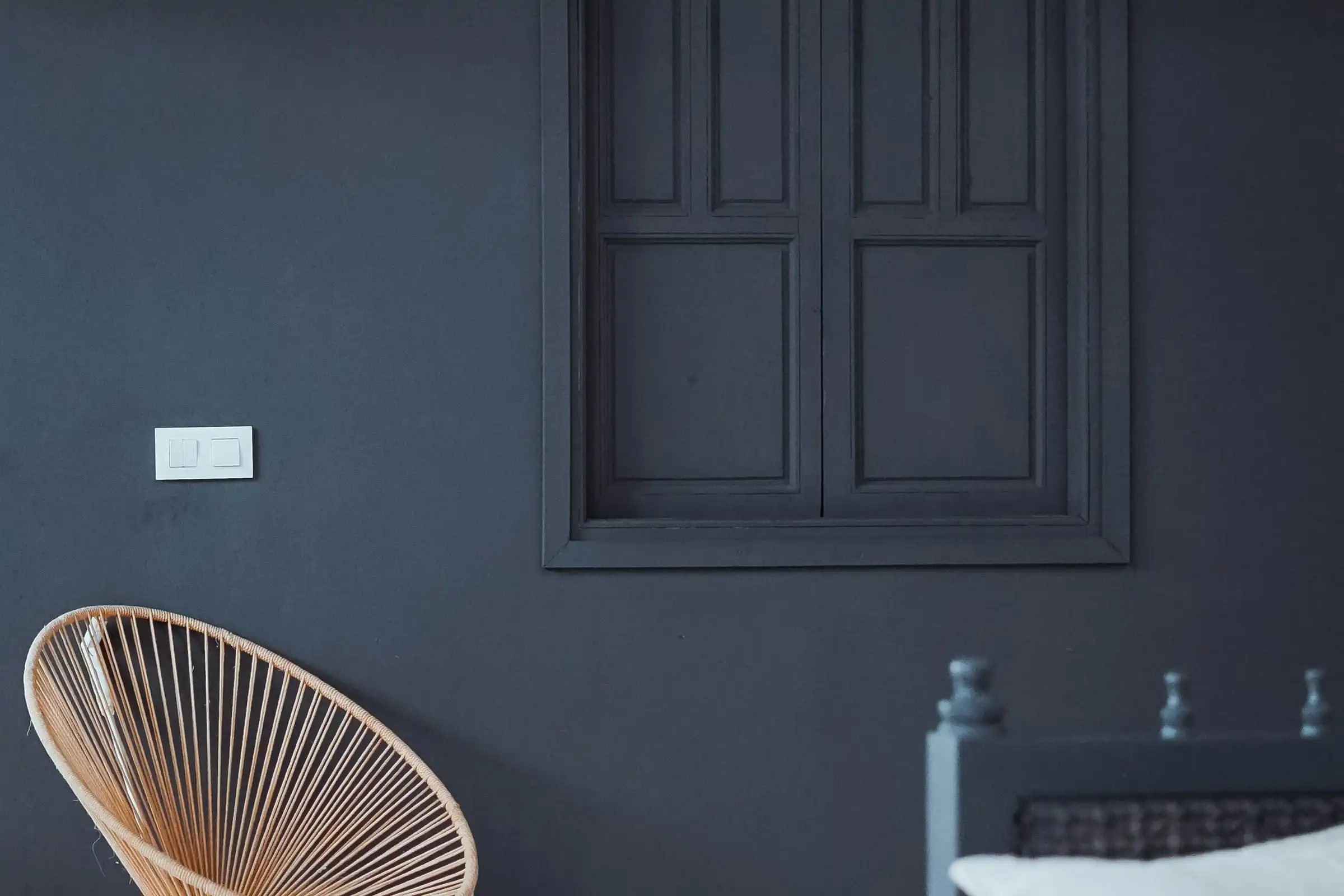 A charcoal-painted wall with panelled timber shutters and a woven chair