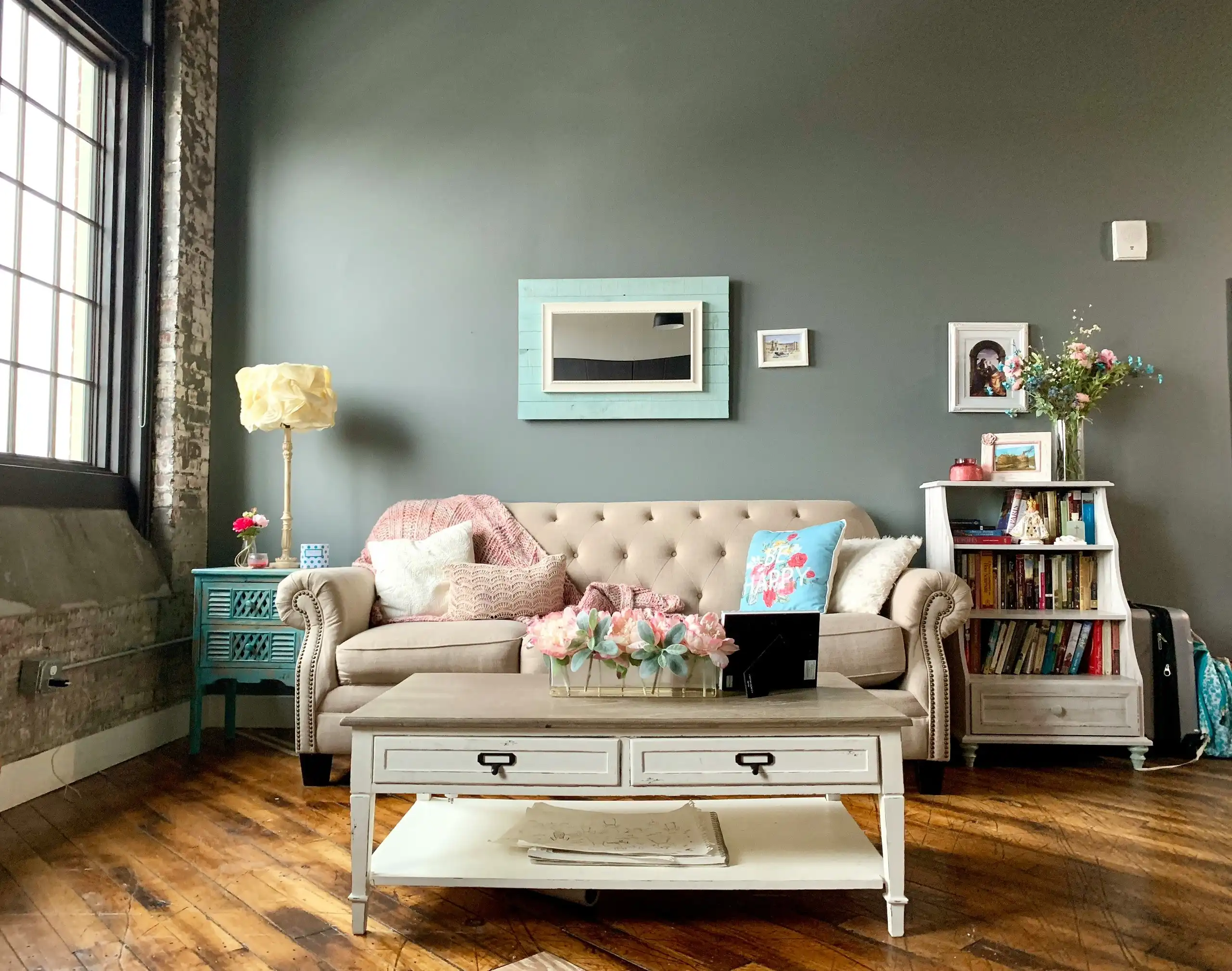 A living room with grey-green walls, a tufted sofa and white painted shelves
