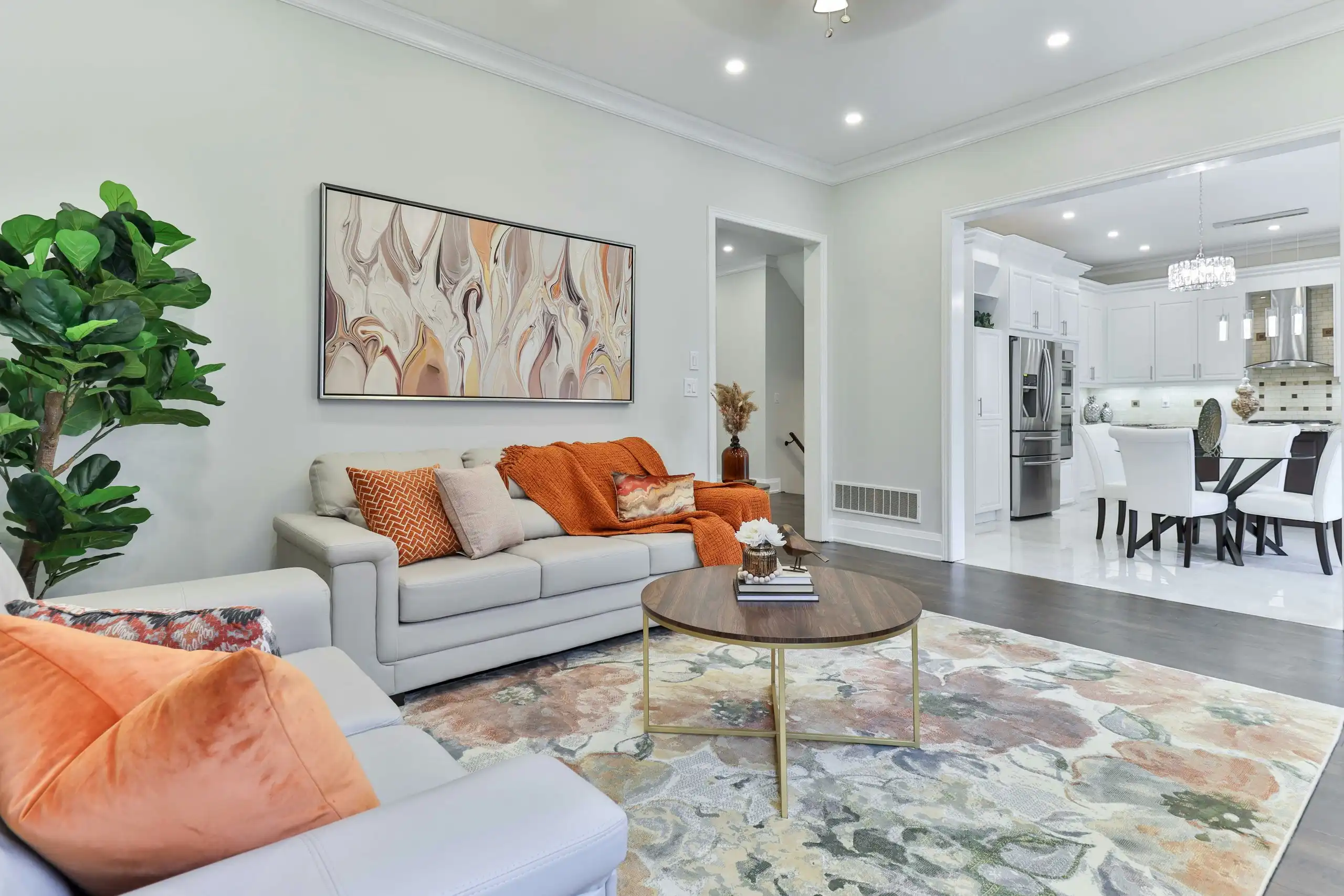 A bright living room with pale walls, a cream sofa with orange cushions and a floral rug