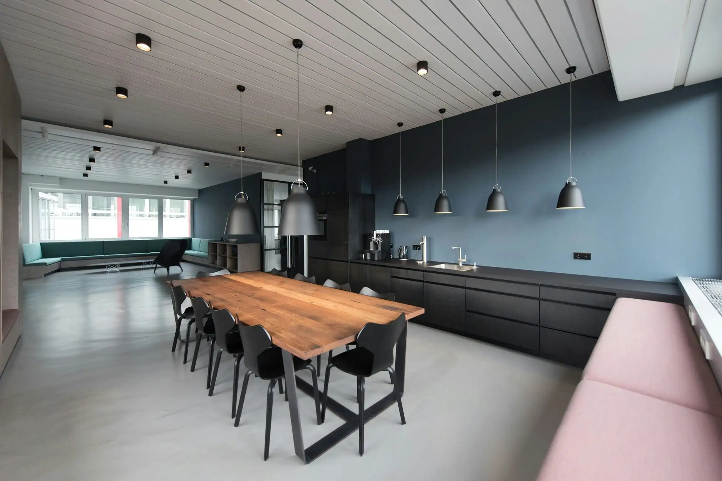 An office kitchen with one wall painted dusty blue above a long timber table