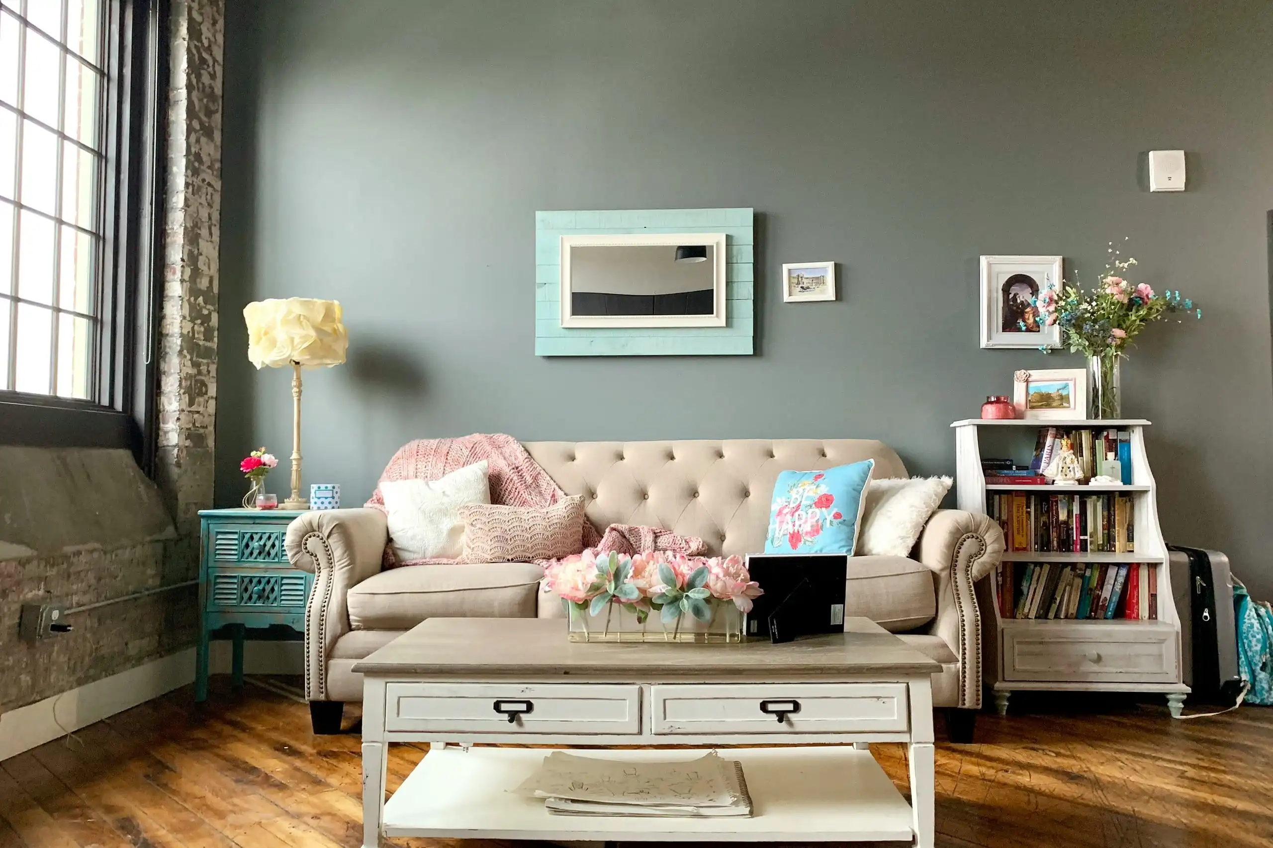 A living room with grey-green walls, a tufted sofa, white bookshelves and a coffee table