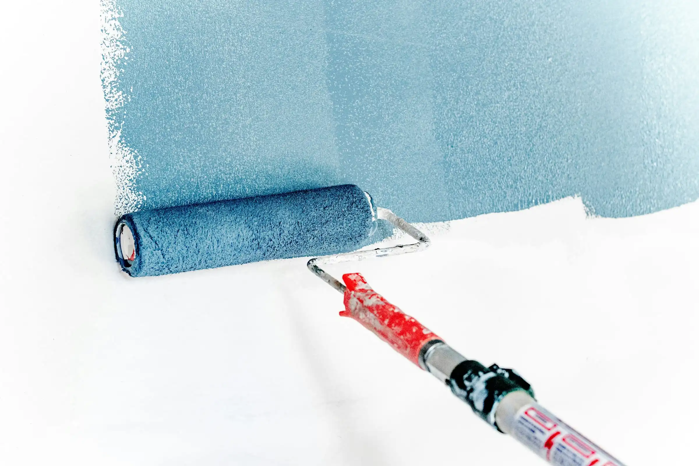 A roller on an extension pole laying blue paint over a white surface